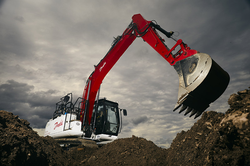 An excavator on a mound of dirt, ready to scoop up a load of dirt.