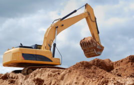 An excavator on a dirt mound lifting dirt.