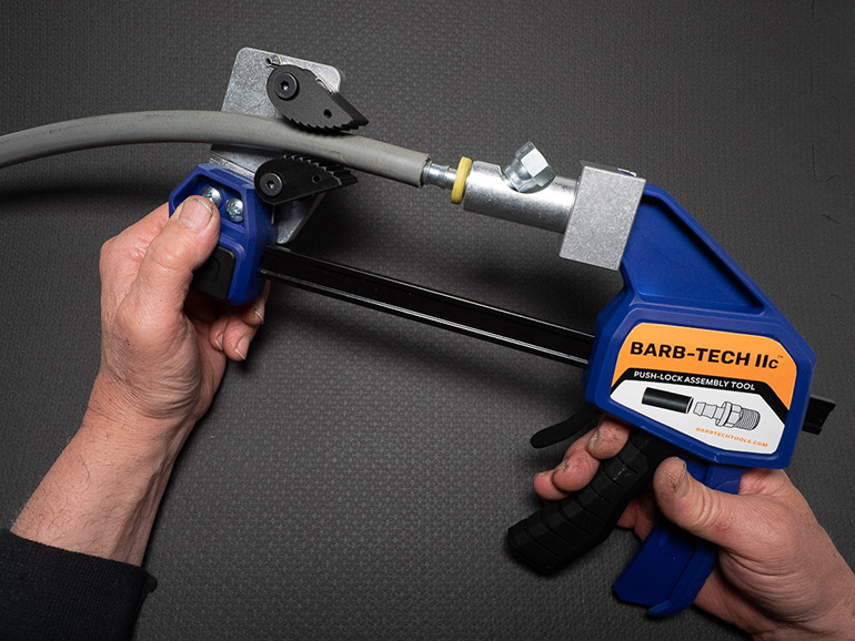 The Barb-Tech device features a mandrel at one end to hold the fittings and jaw-like clamps at the other end. Pushing a lever pushes the fitting into the hose, while the jaw-clamps tightly hold the hose secure as the fitting is pushed into the hose.